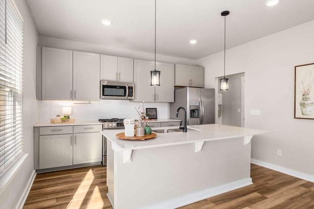 kitchen with sink, a kitchen island with sink, gray cabinetry, stainless steel appliances, and light wood-type flooring