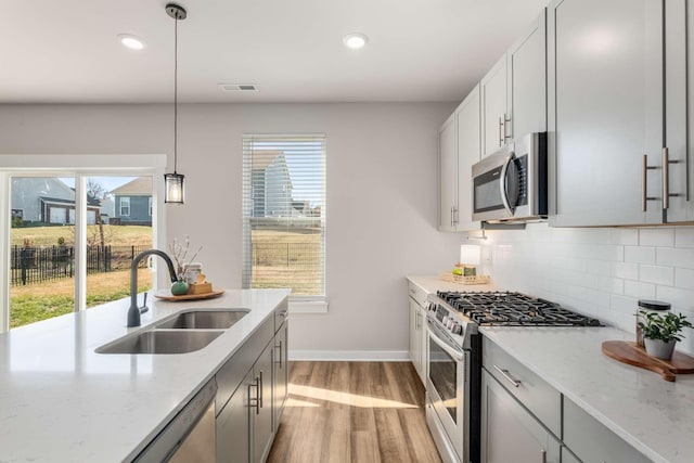 kitchen featuring stainless steel appliances, light stone countertops, sink, and hanging light fixtures