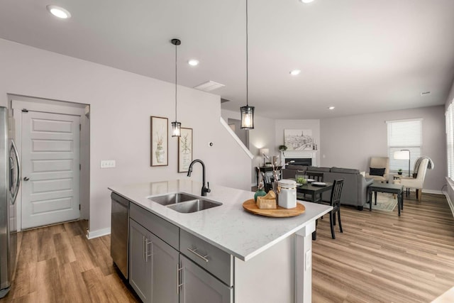 kitchen featuring pendant lighting, sink, gray cabinetry, light stone countertops, and a center island with sink