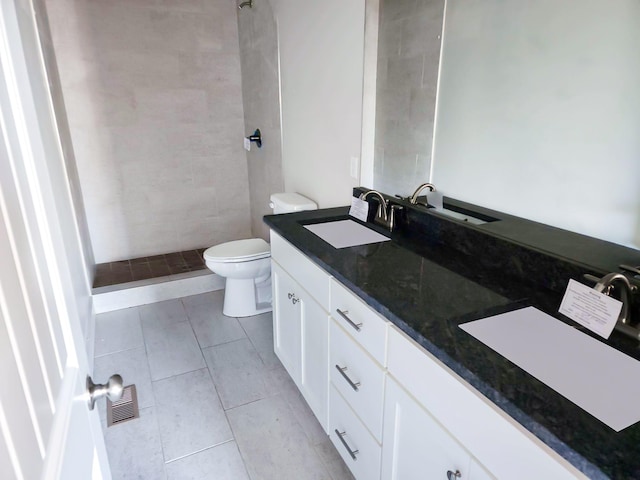 bathroom with tile patterned flooring, vanity, tiled shower, and toilet