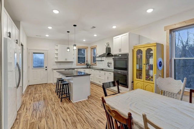 kitchen featuring white cabinetry, fridge, a center island, a kitchen breakfast bar, and decorative light fixtures