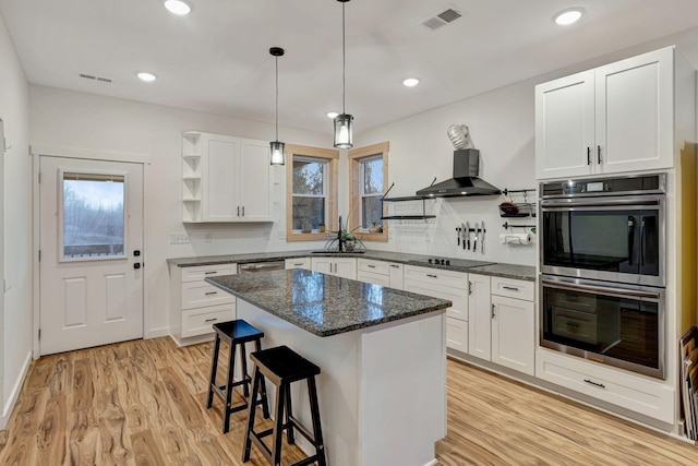 kitchen featuring dark stone countertops, white cabinets, a center island, stainless steel appliances, and wall chimney exhaust hood