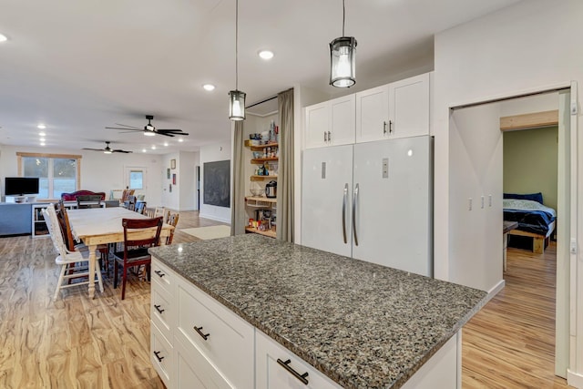 kitchen with white cabinetry, a kitchen island, white fridge, pendant lighting, and dark stone counters