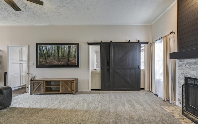 carpeted living room featuring a stone fireplace, a textured ceiling, ornamental molding, ceiling fan, and a barn door