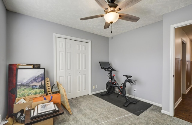 workout area featuring ceiling fan, dark carpet, and a textured ceiling