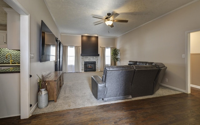 living room with dark wood-type flooring, ceiling fan, a fireplace, ornamental molding, and a textured ceiling