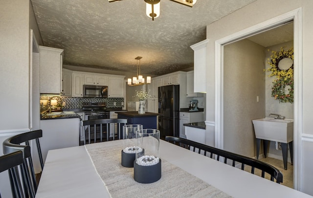 dining area with sink, ceiling fan with notable chandelier, and a textured ceiling