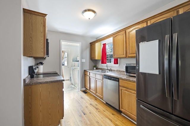 kitchen featuring independent washer and dryer, appliances with stainless steel finishes, sink, and light wood-type flooring