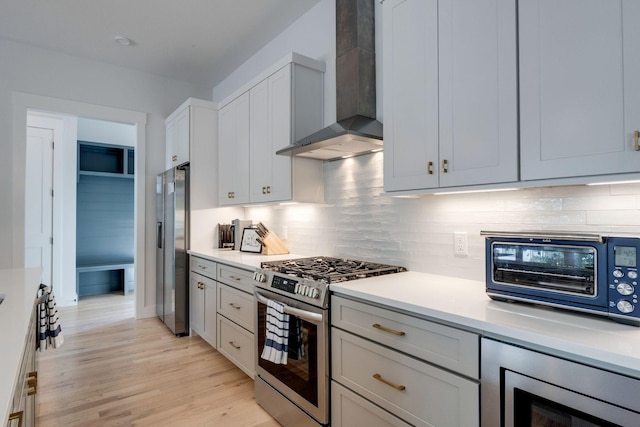 kitchen featuring appliances with stainless steel finishes, backsplash, light hardwood / wood-style floors, and wall chimney exhaust hood