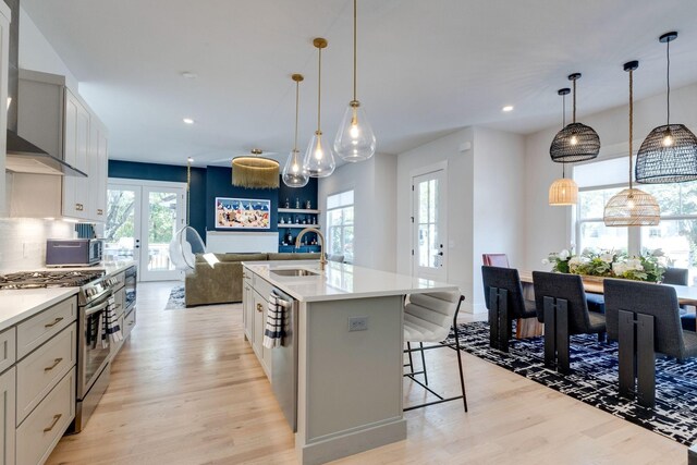 kitchen with stainless steel appliances, hanging light fixtures, sink, and a center island with sink