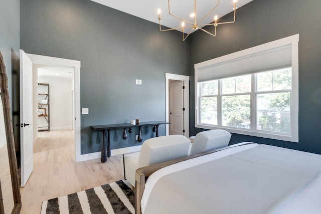 bedroom featuring a towering ceiling, a notable chandelier, and light wood-type flooring