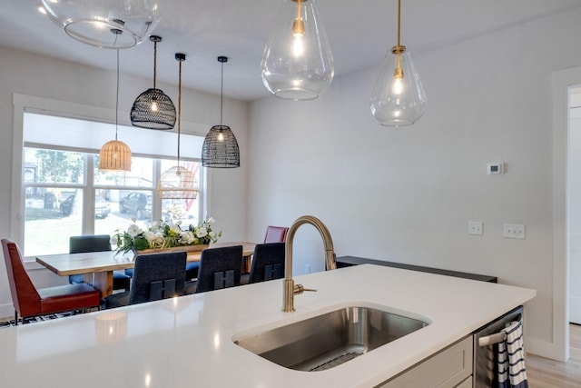 kitchen featuring sink, light hardwood / wood-style flooring, stainless steel dishwasher, and hanging light fixtures