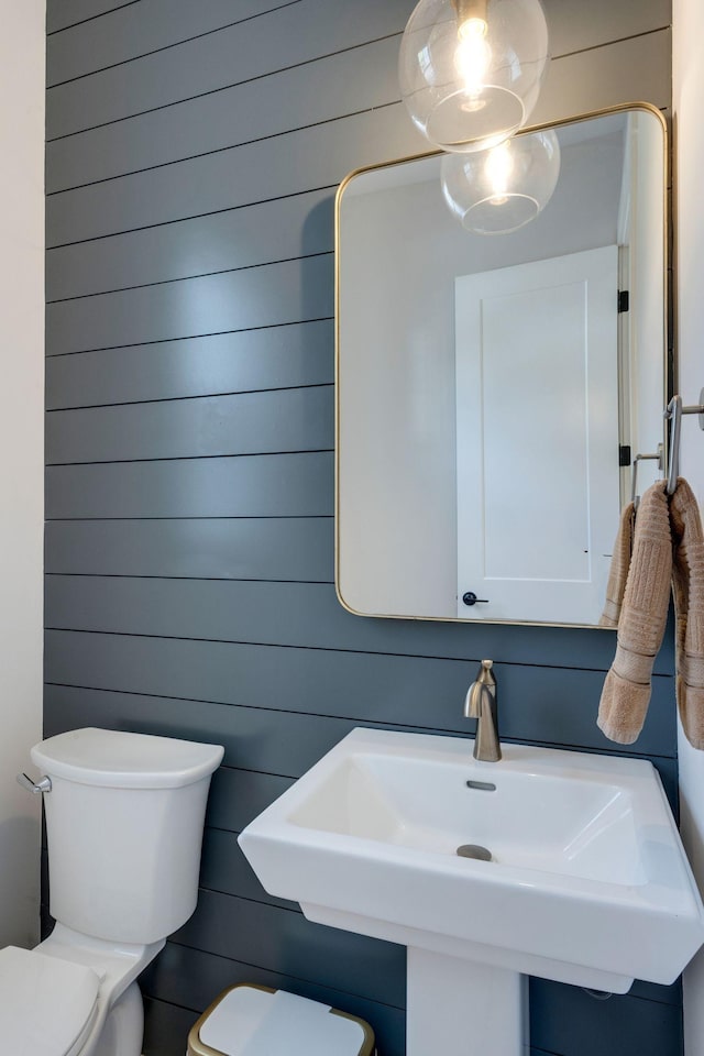 bathroom featuring sink, wooden walls, and toilet