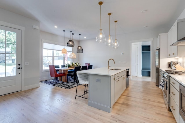 kitchen with sink, a breakfast bar area, appliances with stainless steel finishes, a kitchen island with sink, and hanging light fixtures