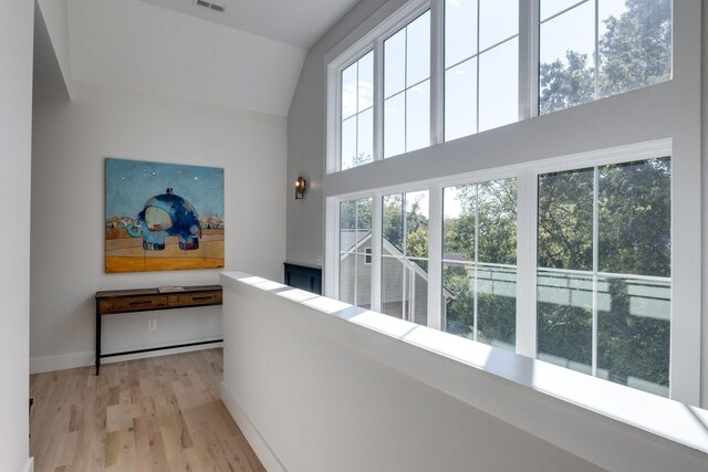 hallway with high vaulted ceiling and light hardwood / wood-style floors