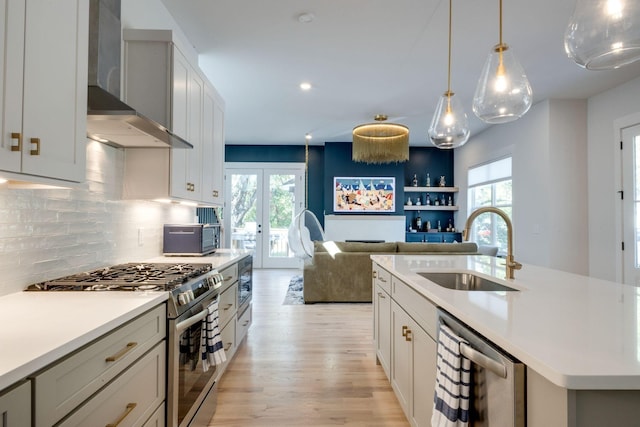 kitchen with sink, a kitchen island with sink, gas stove, french doors, and wall chimney exhaust hood