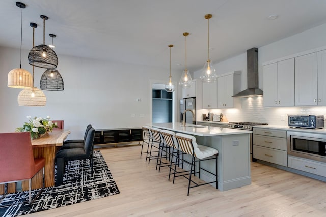 kitchen with wall chimney exhaust hood, sink, an island with sink, pendant lighting, and stainless steel appliances