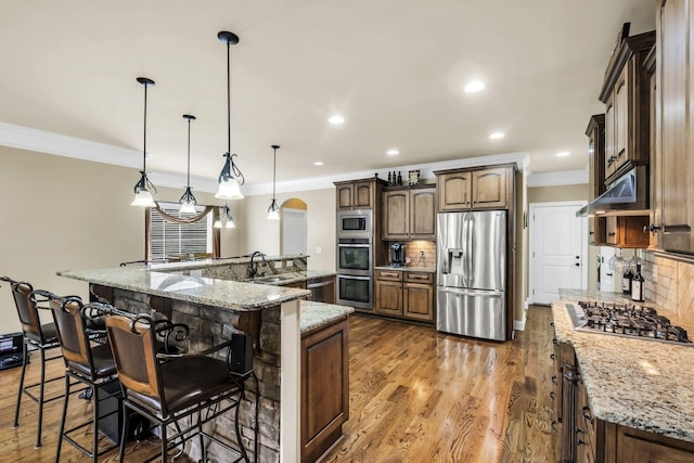 kitchen featuring a breakfast bar, pendant lighting, light stone counters, stainless steel appliances, and a spacious island