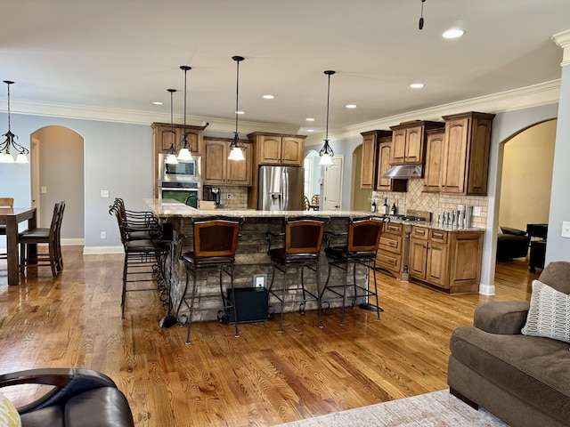 kitchen with decorative light fixtures, a kitchen breakfast bar, a large island with sink, and appliances with stainless steel finishes