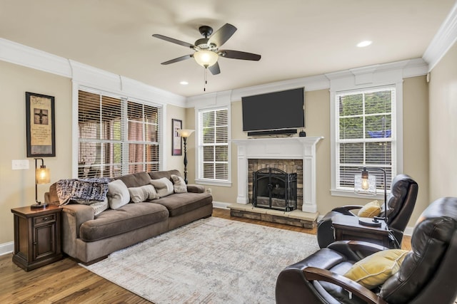 living room with crown molding, ceiling fan, a fireplace, and light hardwood / wood-style flooring