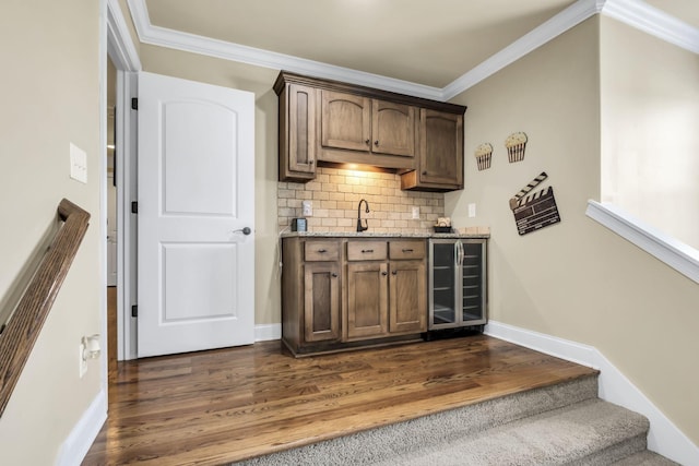 bar with sink, crown molding, dark wood-type flooring, tasteful backsplash, and beverage cooler