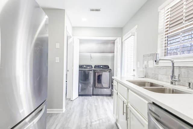 kitchen featuring sink, light hardwood / wood-style flooring, stainless steel appliances, washer and dryer, and white cabinets