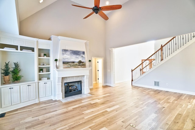 unfurnished living room featuring ceiling fan, a tiled fireplace, high vaulted ceiling, and light hardwood / wood-style flooring