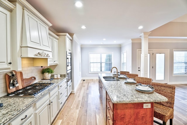 kitchen with decorative columns, sink, a kitchen bar, a kitchen island with sink, and stainless steel appliances