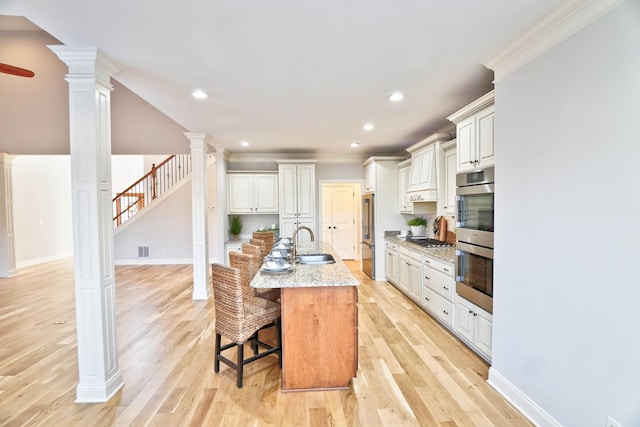 kitchen with sink, a breakfast bar area, a kitchen island with sink, white cabinets, and ornate columns