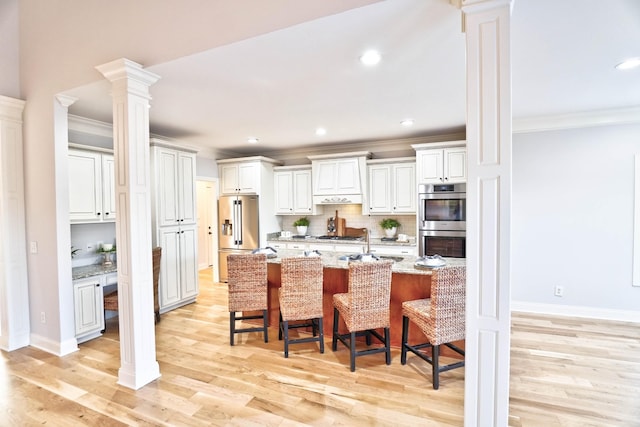 kitchen featuring stainless steel appliances, white cabinetry, a breakfast bar, and decorative columns