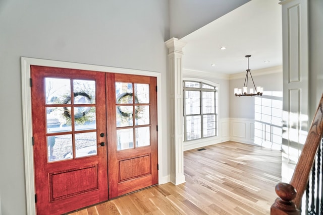 entrance foyer with french doors, crown molding, a chandelier, light wood-type flooring, and decorative columns