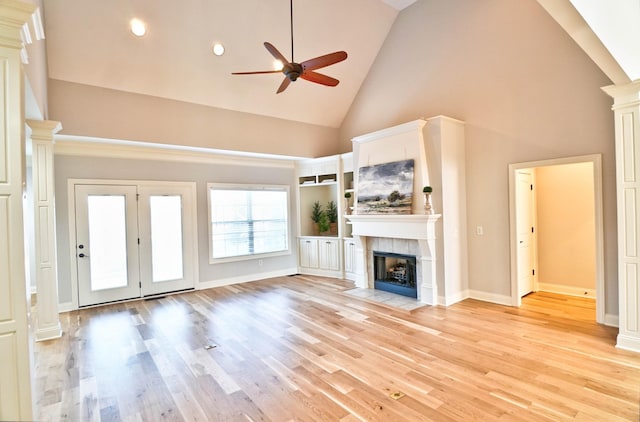 unfurnished living room with light hardwood / wood-style floors, high vaulted ceiling, a tile fireplace, and ornate columns