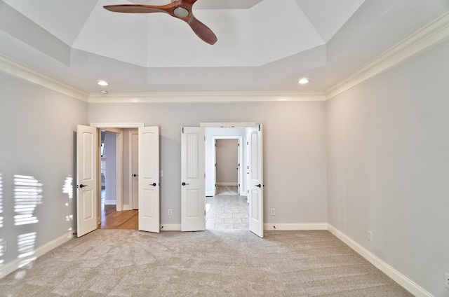 unfurnished bedroom with a raised ceiling, ornamental molding, light colored carpet, and ceiling fan