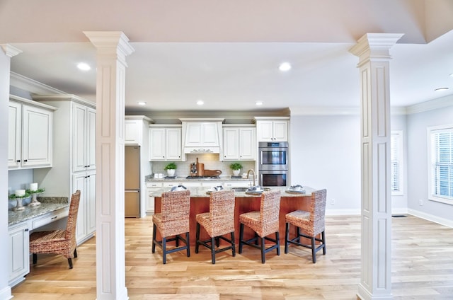 kitchen featuring a breakfast bar, appliances with stainless steel finishes, light stone countertops, white cabinets, and ornate columns