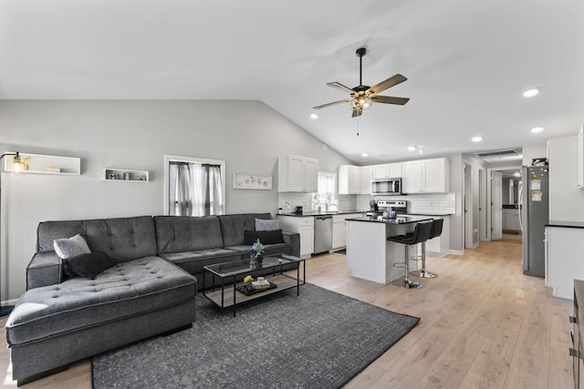 living room featuring ceiling fan, vaulted ceiling, and light wood-type flooring