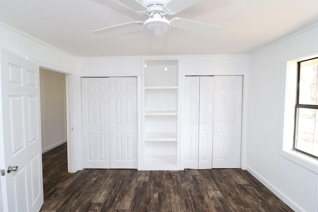 unfurnished bedroom with two closets, dark wood-type flooring, ornamental molding, and ceiling fan