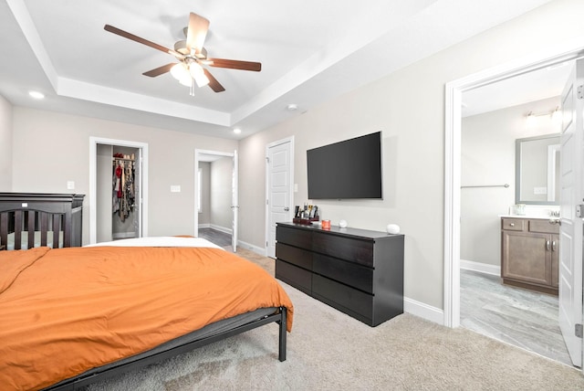 carpeted bedroom featuring a walk in closet, ceiling fan, a tray ceiling, ensuite bath, and a closet