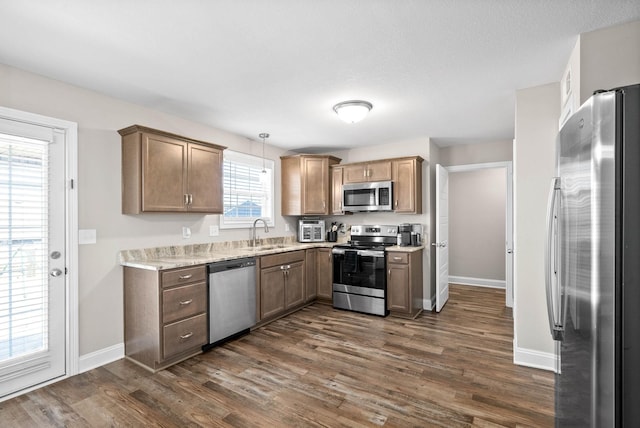 kitchen with dark wood-type flooring, appliances with stainless steel finishes, decorative light fixtures, and sink