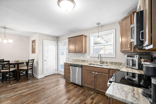 kitchen with pendant lighting, sink, dark wood-type flooring, appliances with stainless steel finishes, and light stone countertops