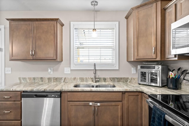 kitchen with sink, decorative light fixtures, light stone countertops, and appliances with stainless steel finishes