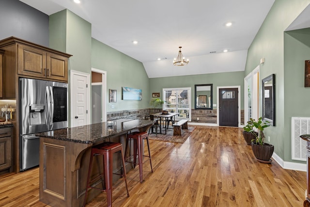 kitchen featuring stainless steel refrigerator with ice dispenser, a breakfast bar, a chandelier, a kitchen island, and dark stone counters