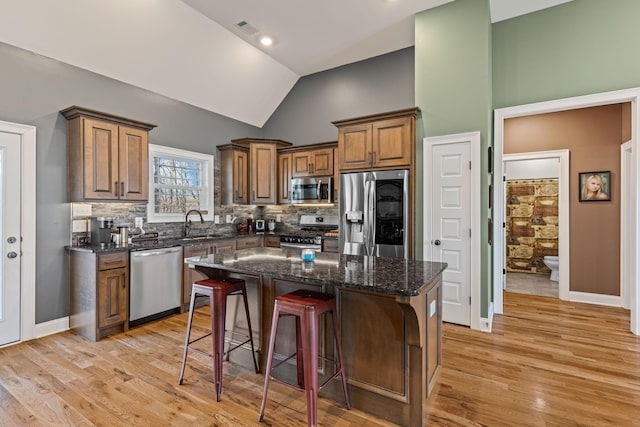 kitchen with a breakfast bar, dark stone countertops, backsplash, stainless steel appliances, and a kitchen island