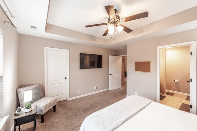 bedroom with ceiling fan, ensuite bathroom, a tray ceiling, and light carpet