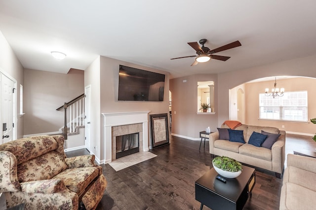 living room with a tiled fireplace, dark wood-type flooring, and ceiling fan