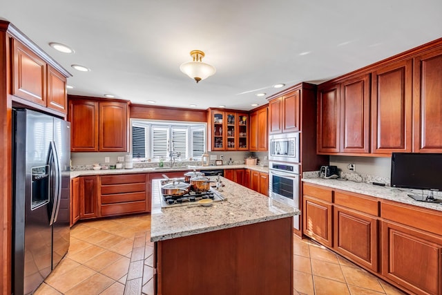 kitchen featuring sink, stainless steel appliances, light stone counters, a kitchen island, and light tile patterned flooring