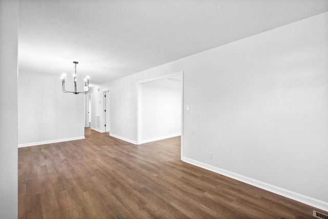 empty room featuring an inviting chandelier and dark hardwood / wood-style floors