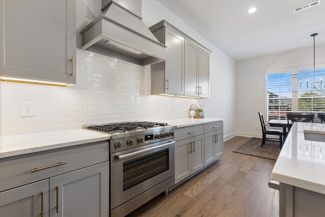 kitchen featuring premium range hood, pendant lighting, stainless steel stove, gray cabinetry, and hardwood / wood-style flooring