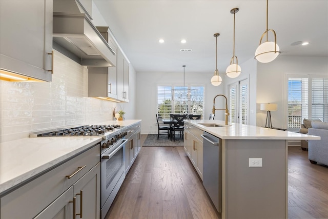 kitchen with sink, gray cabinets, appliances with stainless steel finishes, and a center island with sink