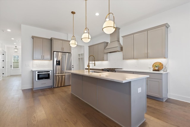 kitchen featuring sink, hanging light fixtures, an island with sink, custom range hood, and stainless steel fridge with ice dispenser