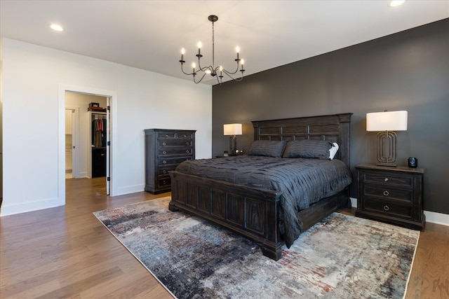 bedroom with wood-type flooring, a walk in closet, and a notable chandelier